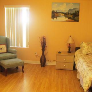 A cozy bedroom featuring a comfortable chair, bedside table with a lamp, and a decorative painting on the wall.