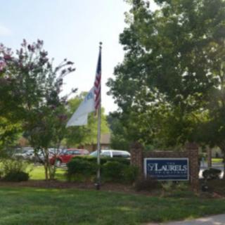 A landscaped area with a sign and flags surrounded by trees.