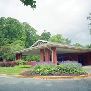 A brick building surrounded by greenery and landscaped plants under a cloudy sky.