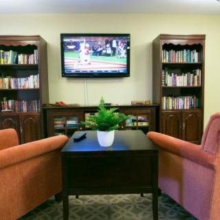 A cozy living room setup with bookshelves, a wall-mounted television, and comfortable chairs around a central table with a plant.