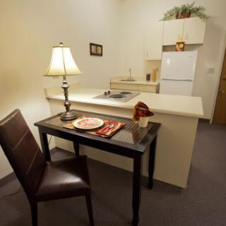 A compact kitchen and dining area with minimalist decor, featuring a small table and chair next to a lamp.