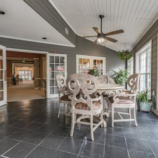 A bright dining area with elegant furniture, ceiling fan, and large windows offering natural light.