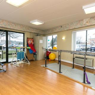 A bright and spacious physical therapy room equipped with exercise bars and colorful fitness balls.
