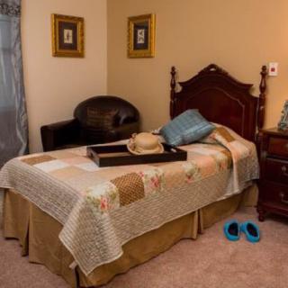 A cozy bedroom with a single bed and a quilt, accompanied by a chair, nightstand, and blue slippers on the floor.