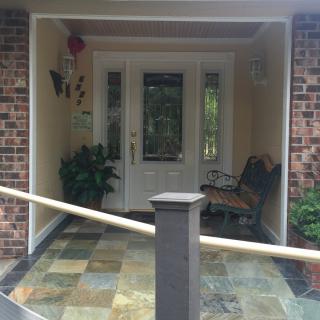 A welcoming front porch with a glass-paneled door, a bench, and potted plants.
