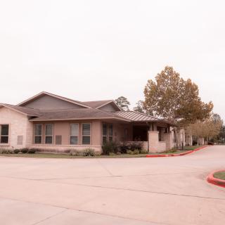 A single-story residential building with a driveway and trees nearby.