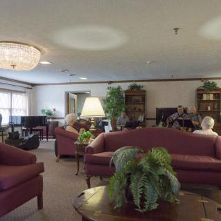 A cozy living room with multiple sofas, a chandelier, and people seated around.