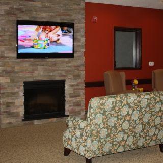 A cozy living room with a stone fireplace, television mounted above, and comfortable seating.