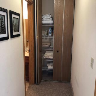 A hallway with a linen closet filled with neatly folded towels and other items.