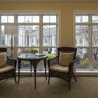 A cozy living room with large windows, featuring two chairs and a small table.