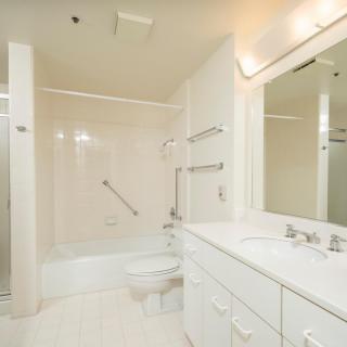 A clean, white bathroom featuring a bathtub, shower, large mirror, and sink.