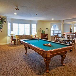 A cozy game room featuring a billiards table and comfortable seating area by the windows.
