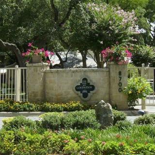 A landscaped garden with a wall and gate, surrounded by lush greenery and trees.