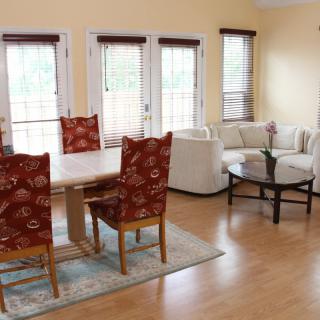 A bright and airy living room with a dining area, featuring wood flooring, large windows, and comfortable seating.