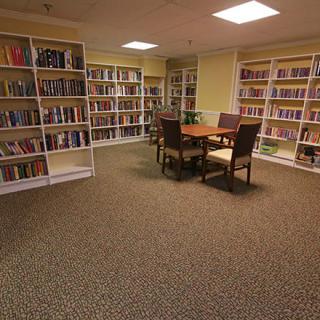 A quiet library room with bookshelves and a reading table surrounded by chairs.