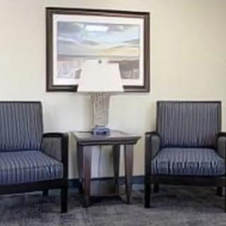 A waiting room with two striped chairs, a side table, a lamp, and a framed picture on the wall.