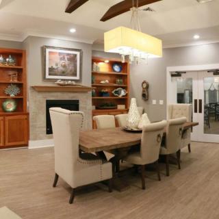 A cozy dining room with a wooden table, upholstered chairs, and a fireplace surrounded by shelves.