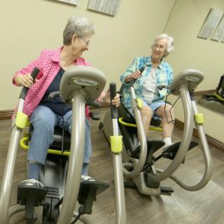 Two elderly women enjoying a workout on fitness machines in a gym.