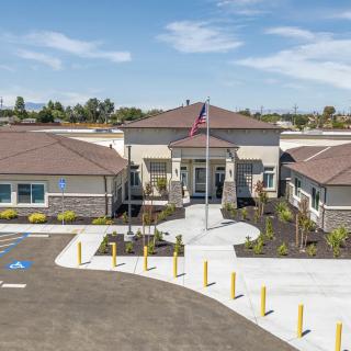 A modern building with a flagpole in front, surrounded by a parking lot and landscaped areas.