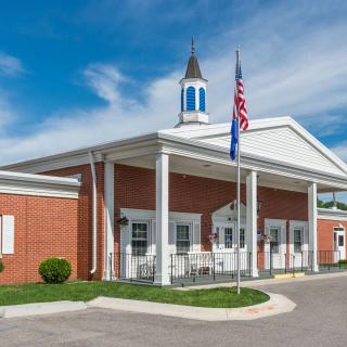 A brick building with a steeple and flagpoles stands under a blue sky.