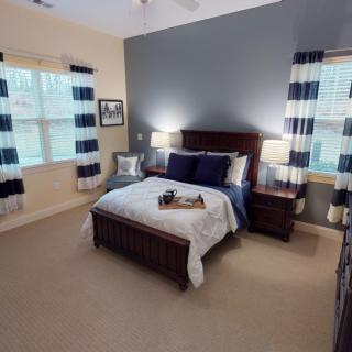 A modern bedroom with a blue and white color scheme, featuring a neatly made bed, matching curtains, and elegant nightstands with lamps.