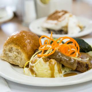 A hearty meal featuring a bread roll, mashed potatoes with gravy, and assorted vegetables.