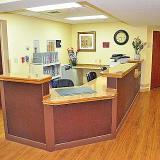 A tidy office reception area with a wooden desk and chairs, featuring organized decorations and ample lighting.