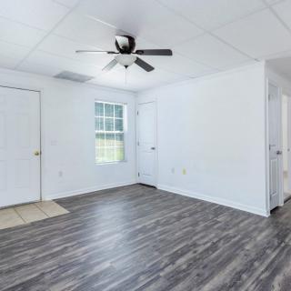 An empty room with wood flooring, a ceiling fan, and white walls.