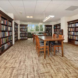A cozy library reading room with bookshelves and a central table surrounded by chairs.