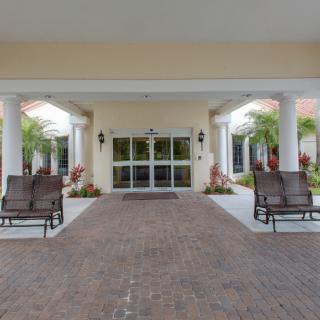 A building entrance with columns, featuring patio chairs and landscaping.