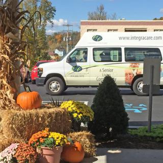 A decorated outdoor display with pumpkins, flowers, and hay bales in front of a parked van on an autumn day.