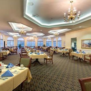 An elegant dining room with neatly set tables and chandeliers overhead.