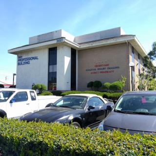 A commercial office building with vehicles parked in front and greenery surrounding the area.