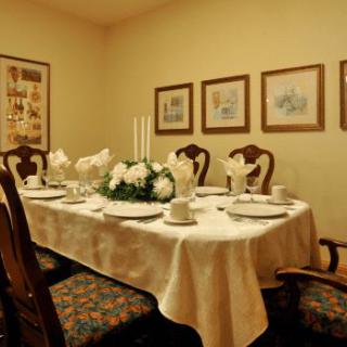 A formal dining room set with a tablecloth, place settings, candles, and a floral centerpiece.