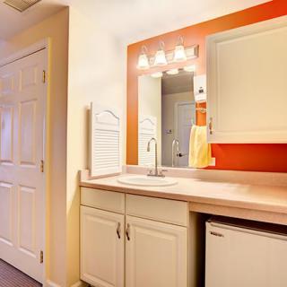 A modern bathroom with a sink, mirror, and cabinetry against an orange accent wall.