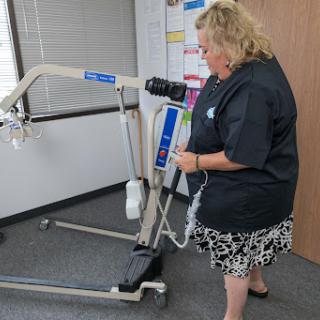 A healthcare professional demonstrating the use of a patient lift in a medical office.
