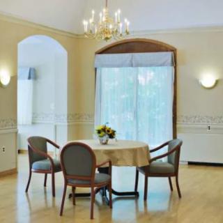 A bright and elegant dining room featuring a round table with four chairs, illuminated by a chandelier above.
