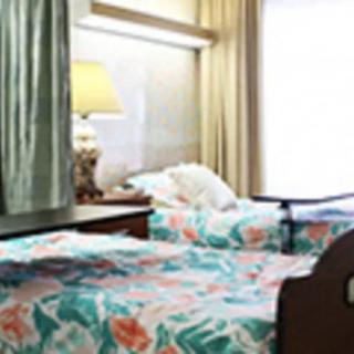 A hospital room featuring two beds with floral bedspreads and a bedside lamp.