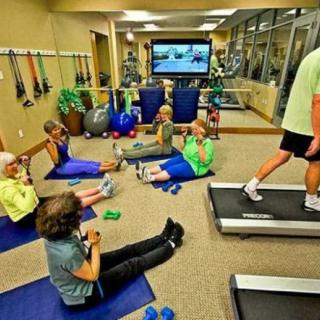 Group of people exercising on mats and using treadmills in a gym.