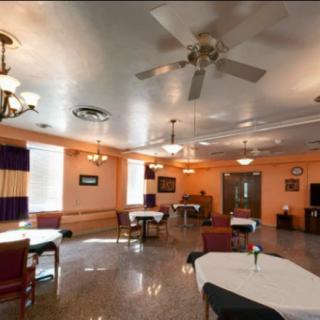 A spacious dining area with tables and chairs, featuring elegant lighting and a ceiling fan.