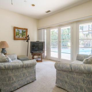 A cozy living room with sofas, a TV, large windows, and a view of the pool.