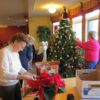 Seniors decorating a Christmas tree indoors with ornaments and festive decorations.