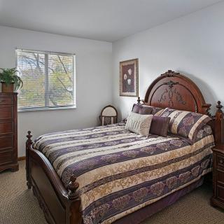 A cozy bedroom with a wooden bed and dresser, featuring patterned bedding and a window with outdoor views.