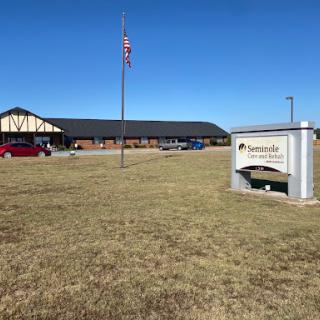 A view of a building with an American flag in front, accompanied by signage and parked cars on a clear day.