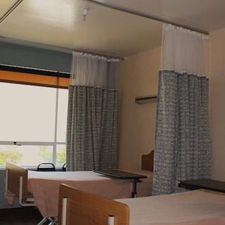 A hospital room with two beds separated by privacy curtains.