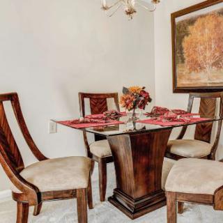 A stylish dining room with a glass-top table and four wooden chairs, adorned with elegant decor and artwork.