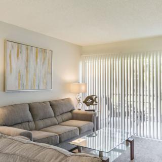 A modern living room with a comfortable grey sofa and contemporary artwork, softly illuminated by a table lamp near window blinds.