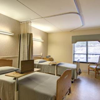 A clean and well-lit hospital patient room with two beds and a window.