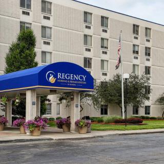 The exterior entrance of a hotel with a blue awning, surrounded by landscaping and flags.