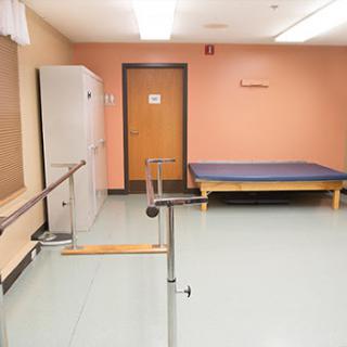 A rehabilitation therapy room featuring a ballet barre and a bed, designed for patient exercises and recovery.